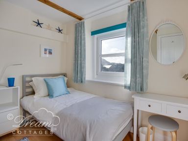 A bedroom with a single bed, bedside table with a lamp, window with curtains, dressing table with a stool and round mirror at Ammonite Cottage Fortuneswell Portland