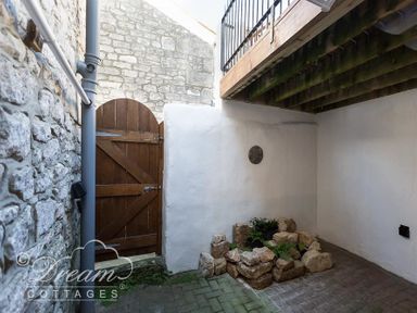 An outdoor patio area with stone walls wooden gate and a small rock garden under a wooden balcony at Ammonite Cottage in Fortuneswell Portland