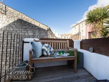 An outdoor seating area with a wooden bench and cushions on a wooden deck at Ammonite Cottage in Fortuneswell Portland