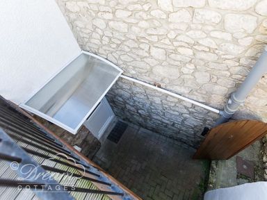 A stone walled outdoor area with a wooden gate and a white door under a clear awning at Ammonite Cottage in Fortuneswell Portland
