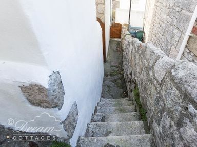 An outdoor stone staircase between stone and white plaster walls leading to a wooden gate at Ammonite Cottage in Fortuneswell Portland
