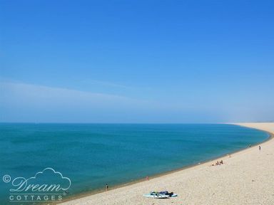 A curved sandy beach with a few people near the water and kayaks on the shore at Ammonite Cottage in Fortuneswell Portland