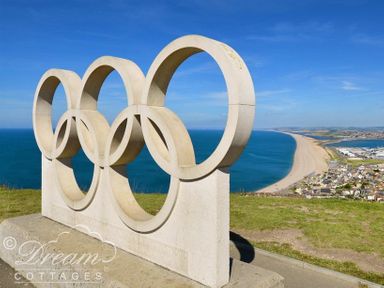 A sculpture of the Olympic rings on a hill overlooking a curved beach and town at Ammonite Cottage Fortuneswell Portland