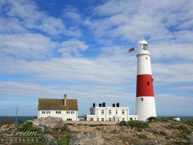 A lighthouse with a red band and adjacent white buildings on a rocky shore under a partly cloudy sky at Ammonite Cottage Fortuneswell Portland