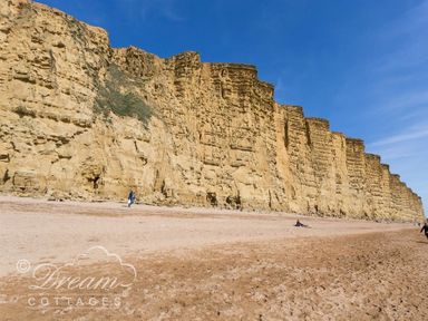 A sandy beach with tall yellow cliffs and a few people walking and sitting at Ammonite Cottage in Fortuneswell Portland