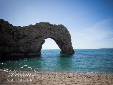 A natural rock arch extending over the sea with a sandy beach in the foreground at Ammonite Cottage in Fortuneswell Portland