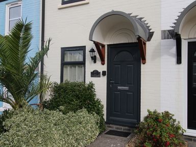 Front door of a house with a black door and curved awning surrounded by plants at Anvil House Brewers Quay Harbour