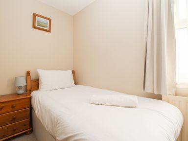 A small bedroom with a single bed a wooden nightstand and a window with curtains at Anvil House Brewers Quay Harbour