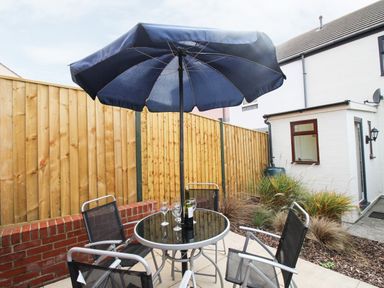 An outdoor patio with a round table and four chairs under a large blue umbrella and a bottle with glasses on the table at Anvil House in Brewers Quay Harbour