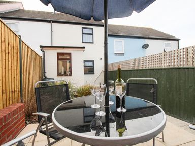 A backyard patio with a round glass table a bottle of wine four wine glasses and four chairs at Anvil House in Brewers Quay Harbour