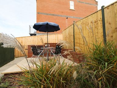 A patio area with a table and four chairs under a blue umbrella surrounded by wooden fences at Anvil House in Brewers Quay Harbour