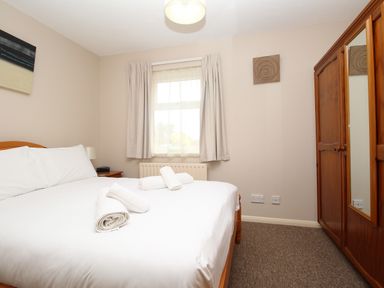 A bedroom with a bed with white linens and rolled towels a wooden wardrobe with mirrored door and a window with curtains at Anvil House in Brewers Quay Harbour