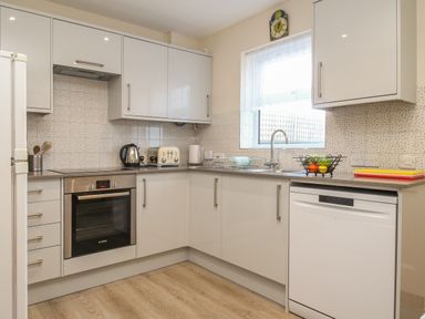 A kitchen with white cabinets a built in oven a kettle a toaster and a dishwasher at Anvil House in Brewers Quay Harbour