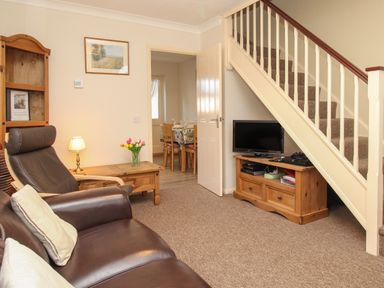 A living room with a brown leather sofa and armchair wooden furniture and a television under the stairs at Anvil House in Brewers Quay Harbour