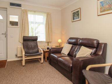 A living room with a leather sofa two armchairs a wooden side table with a lamp and wine glasses at Anvil House in Brewers Quay Harbour