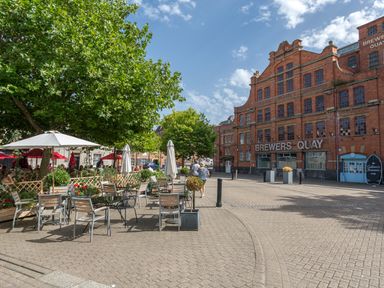 An outdoor seating area with tables and umbrellas near a large brick building labeled Brewers Quay at Brewers Quay Harbour