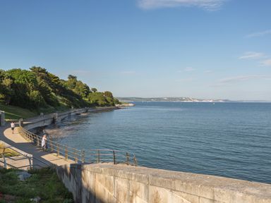 A coastal pathway with people walking and trees on one side and the sea on the other at Anvil House in Brewers Quay Harbour