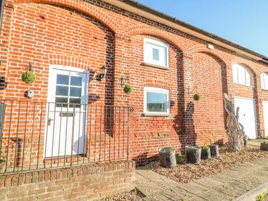 The exterior of a brick building with a white door and windows with hanging plants and potted plants at Barley Mews Brewers Quay Harbour