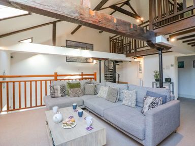 A living room with a large grey sectional sofa and a wooden coffee table with tea set and cupcakes at Barley Mews Brewers Quay Harbour