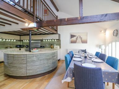 A kitchen with a curved island and dining table set for eight with blue chairs at Barley Mews in Brewers Quay Harbour