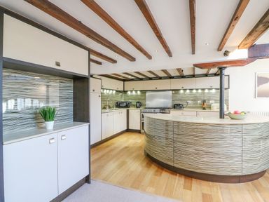 A kitchen with wooden beams on the ceiling and a curved island at Barley Mews in Brewers Quay Harbour