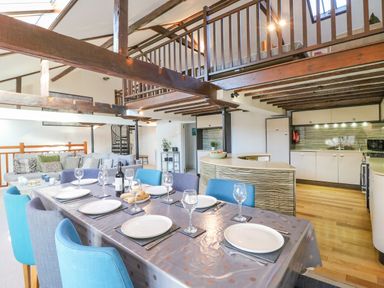 A dining table set with plates and glasses in an open plan kitchen and living area with wooden beams at Barley Mews in Brewers Quay Harbour