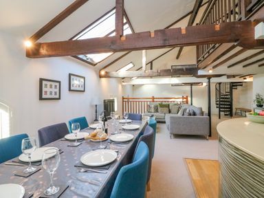 A dining area with a table set for six and a living room with a large grey sofa under exposed beams at Barley Mews in Brewers Quay Harbour