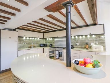 A kitchen with wooden ceiling beams a curved countertop a stove and a bowl of fruit at Barley Mews Brewers Quay Harbour