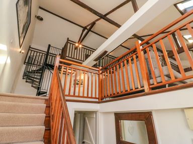 An interior view of a living space featuring carpeted stairs with wooden railing leading to a second floor with wooden balustrades and exposed ceiling beams at Barley Mews Brewers Quay Harbour