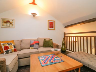 A sitting area with a beige sofa colorful cushions a wooden coffee table with a board game and a banquette at Barley Mews in Brewers Quay Harbour