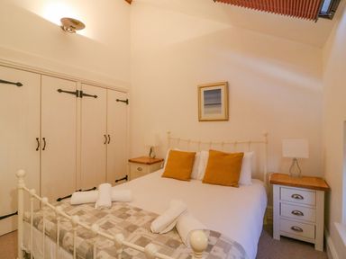 A bedroom with a bed with mustard pillows bedside tables with lamps and a large wardrobe at Barley Mews in Brewers Quay Harbour