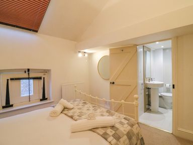 A bedroom with a bed and rolled towels next to a small window and an open door leading to a bathroom at Barley Mews in Brewers Quay Harbour