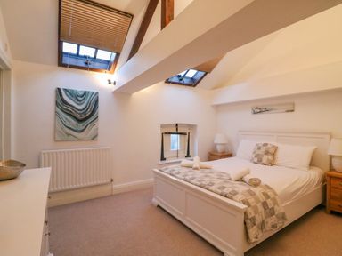 A bedroom with a double bed two bedside tables with lamps skylight windows and paintings at Barley Mews in Brewers Quay Harbour