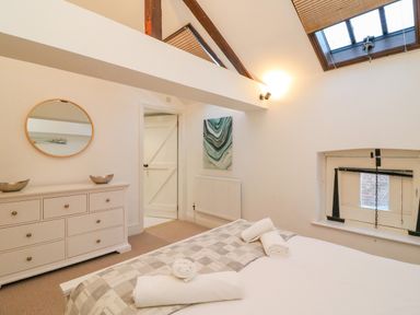 A bedroom with a bed with rolled towels a dresser with two bowls a round mirror a painting a door and a skylight window at Barley Mews in Brewers Quay Harbour