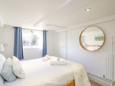 A bedroom with a bed with pillows and towels near a window with blue curtains and a round mirror on the wall at Barley Mews in Brewers Quay Harbour