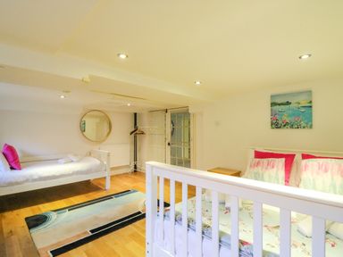A bedroom with two white beds wooden floor a colorful rug round wall mirror and a painting on the wall at Barley Mews Brewers Quay Harbour