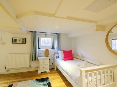 A small bedroom with a single bed a bedside table with a lamp and a mirror on the wall at Barley Mews in Brewers Quay Harbour
