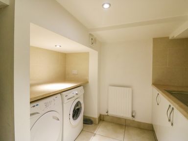 A laundry room with a washing machine and dryer under a countertop next to a radiator at Barley Mews in Brewers Quay Harbour