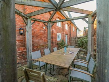 An outdoor dining area with a wooden table and chairs under a wooden pergola beside a brick building at Barley Mews in Brewers Quay Harbour