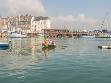 A harbor with boats docked and people rowing a small boat at Barley Mews in Brewers Quay Harbour
