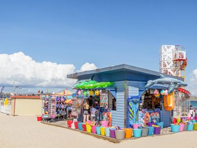 A beachside kiosk selling inflatable toys and beach accessories with colorful buckets and a climbing structure in the background at Barley Mews in Brewers Quay Harbour