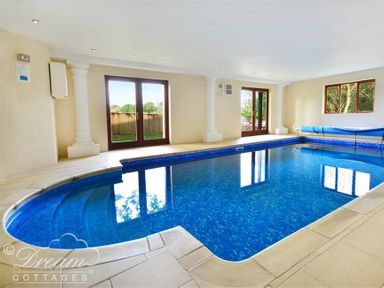 An indoor swimming pool with steps leading into the water and windows showing an outdoor view at Baytree Lodge in Osmington