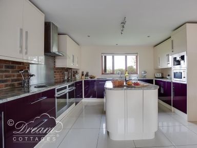 A kitchen with white and purple cabinets a central island and a window at Baytree Lodge in Osmington