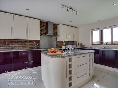 A kitchen with white and purple cabinets a central island with wine glasses and a basket of bread at Baytree Lodge in Osmington