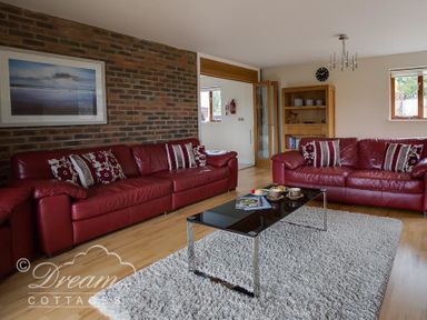 A living room with two red leather sofas a black coffee table on a gray rug and a wooden bookcase at Baytree Lodge in Osmington