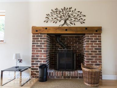 A brick fireplace with a wooden mantel a metal fireguard a black firewood container and a wicker basket at Baytree Lodge in Osmington