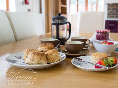 A wooden dining table with plates of scones cups and a French press coffee maker at Baytree Lodge in Osmington