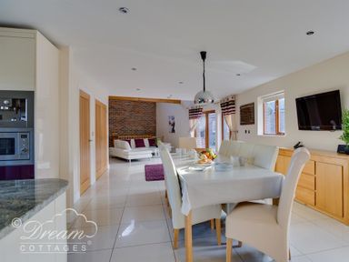 A dining area with a table and chairs next to a living room with a sofa and brick wall at Baytree Lodge in Osmington