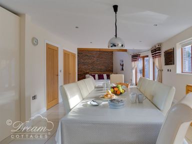 A dining room with a table set with plates cups and fruit bowl and white chairs at Baytree Lodge in Osmington
