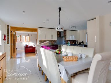 A dining area with a table and chairs next to a kitchen and a sitting room in the background at Baytree Lodge in Osmington